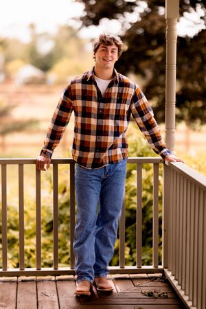 A person in plaid and jeans strikes various poses on a white front porch during a photo session.