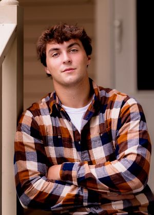 A person in a brown plaid shirt poses against white columns in a casual portrait series.