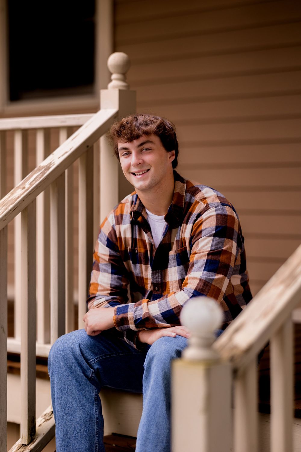A person in casual attire sits relaxed on white porch steps during an outdoor portrait session.