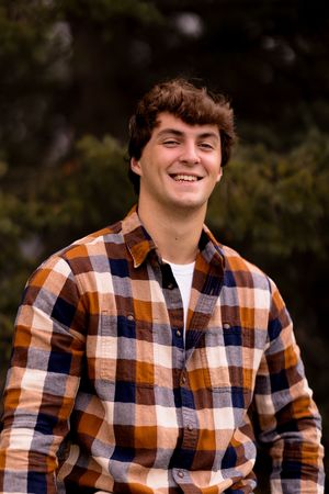 A person in an orange and navy plaid shirt smiles during an outdoor portrait session.