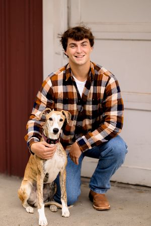 A person in plaid shirt and jeans poses with a beagle mix dog on a concrete driveway.