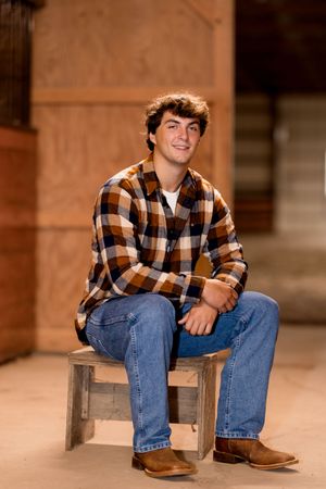 A casual portrait on a wooden bench wearing jeans and a plaid shirt.