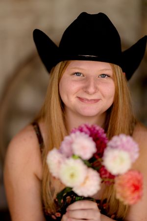 Young person in black cowboy hat holds colorful bouquet of flowers while smiling.
