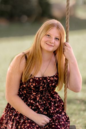Person in floral dress sits on rope swing outdoors during summer photoshoot.