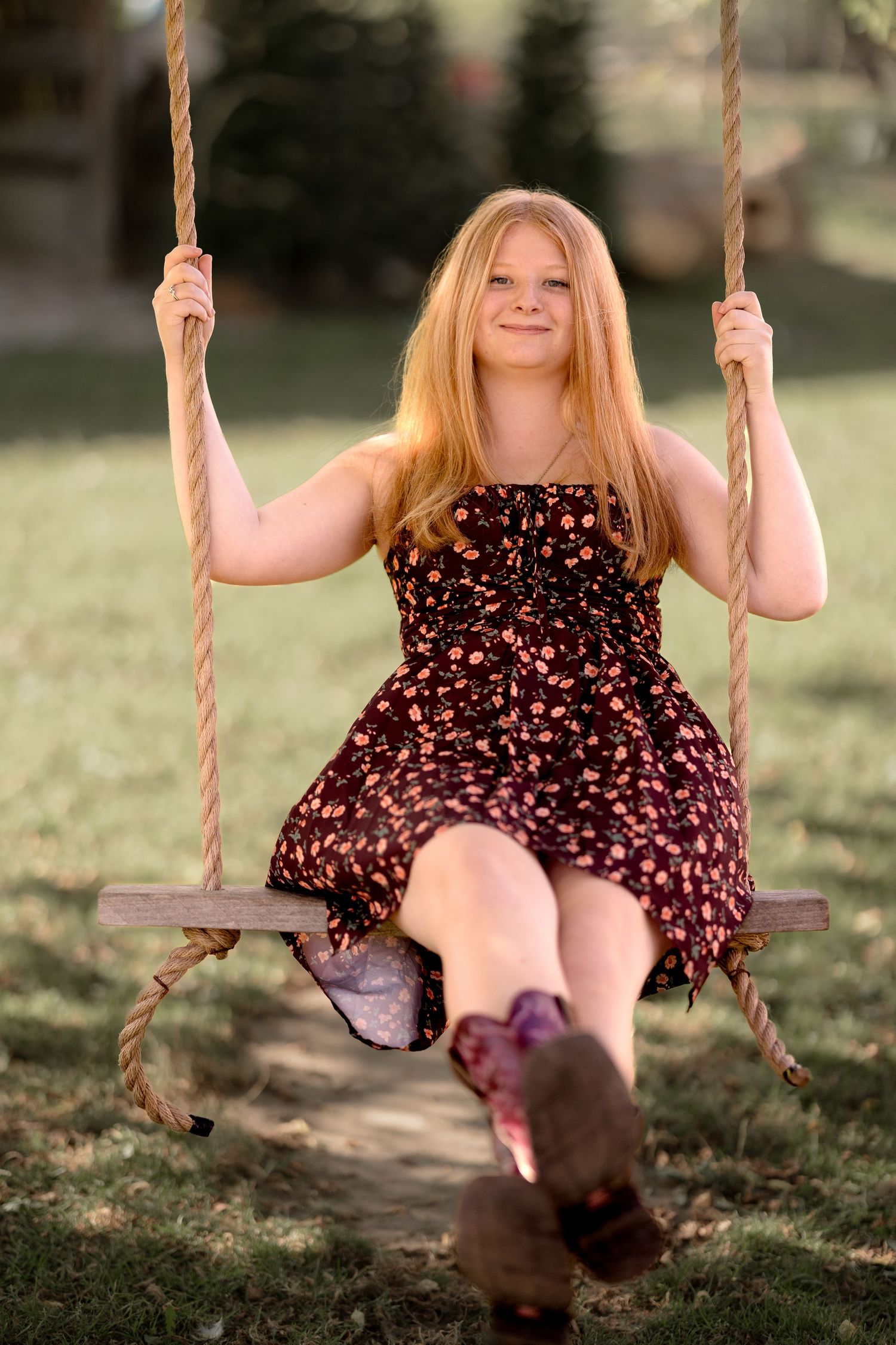A person wearing a floral dress enjoys swinging on a rope swing in a sunny outdoor setting.