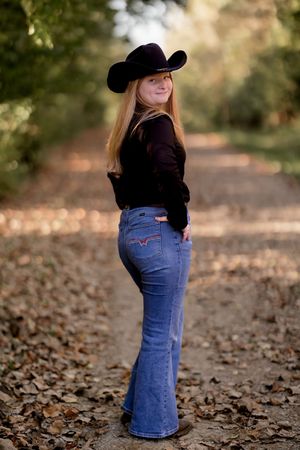 Stylish casual wear with blue jeans and a black top complemented by a western hat in an autumn setting.
