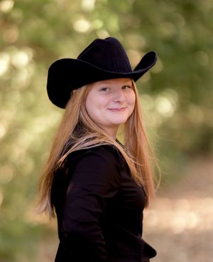 A casual western-inspired portrait featuring a black cowboy hat and blonde hair against a soft natural background.