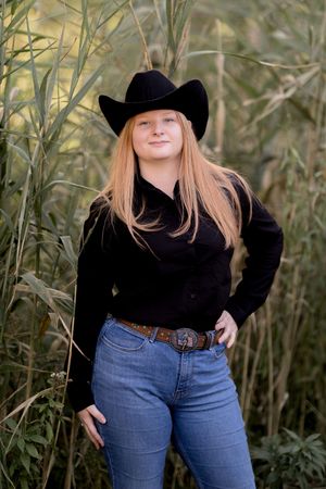 Western-inspired outdoor photoshoot with denim jeans and black turtleneck against tall grass backdrop.
