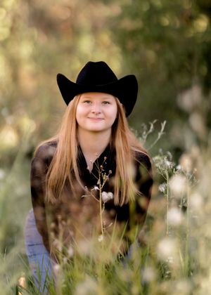 Autumn outdoor portrait with cowboy hat and black turtleneck surrounded by natural foliage.
