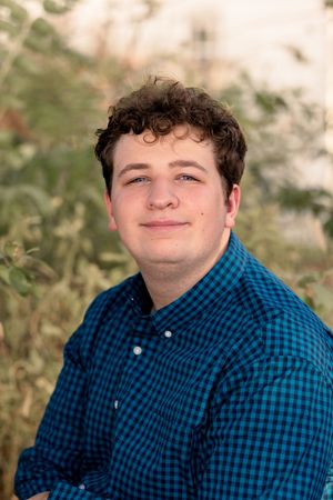 Portrait against natural background showing person in blue checkered collared shirt.