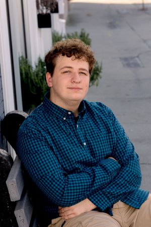 Person in blue plaid shirt sitting casually against light colored wall.