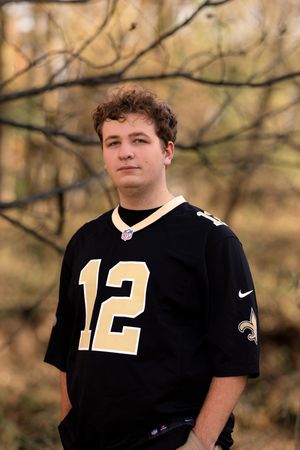 A person wearing a black New Orleans Saints #12 Nike jersey poses outdoors in autumn.