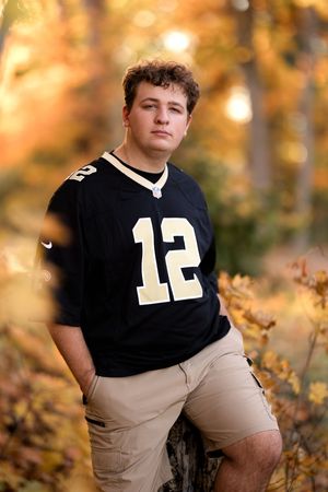 Athletic portrait in a black #12 jersey against golden autumn foliage.
