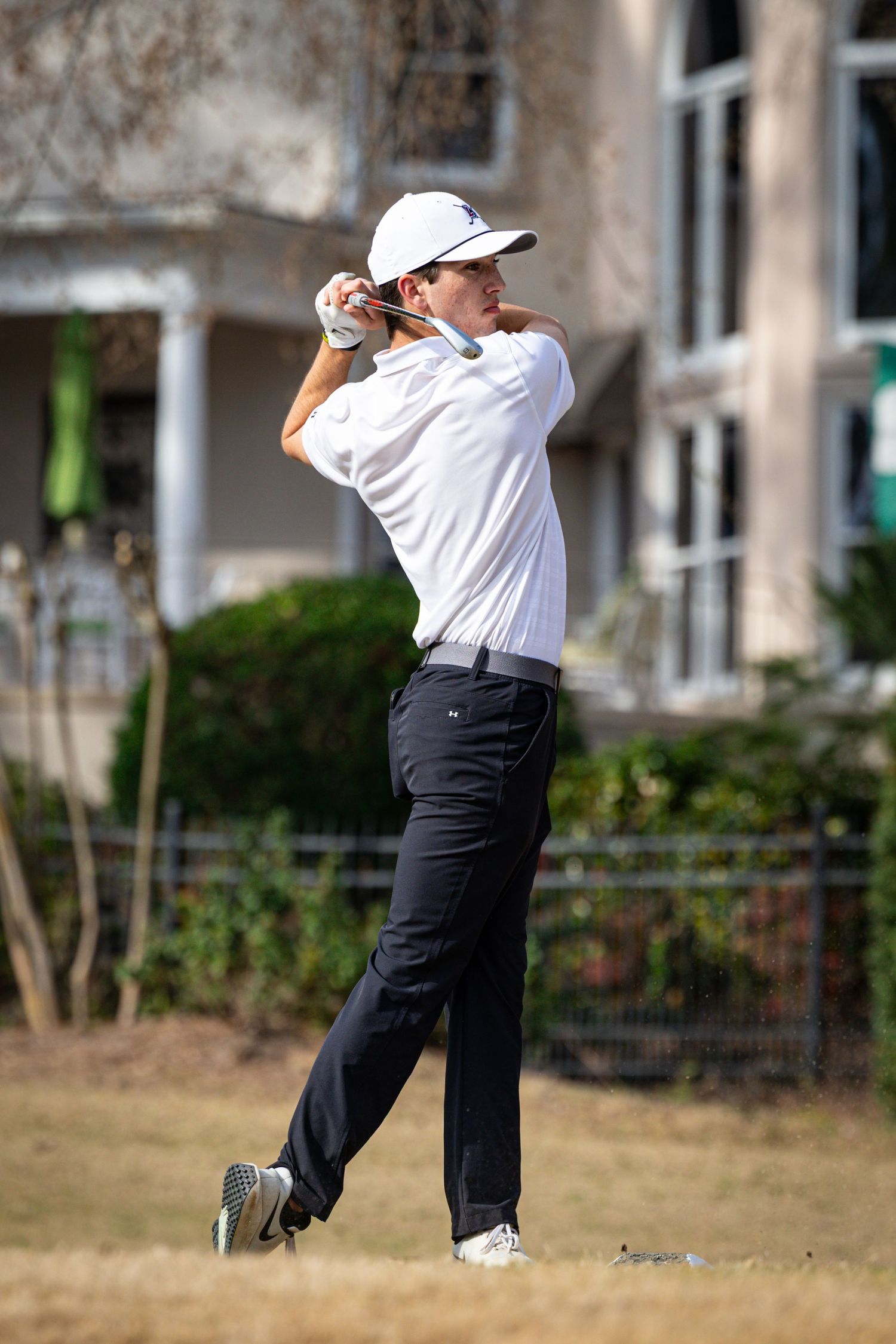 Golfer in white polo shirt swings club during follow-through motion.