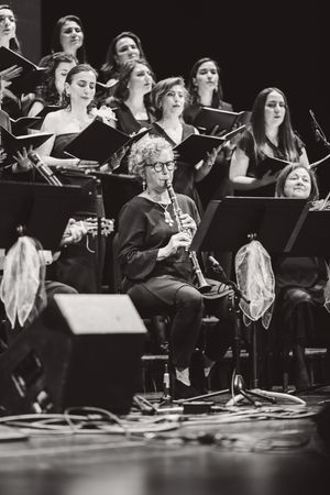 A black and white concert photo showing a clarinetist performing in front of a choir during a classical music performance.