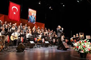 A choir and orchestra performs on stage with Turkish flags and decorative floral arrangements.