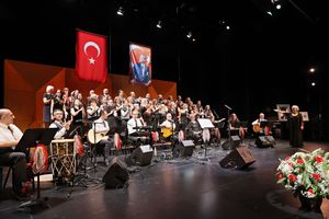 Orchestra performs on stage with Turkish and American flags hanging above during a cultural music concert.