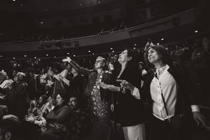 Black and white photo of concert audience members standing and cheering enthusiastically during a live performance.