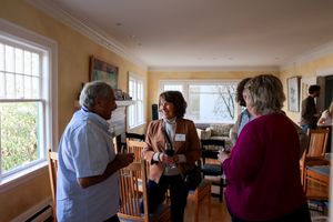 People conversing in a bright sunlit room with yellow walls and large windows, creating a warm and inviting atmosphere.