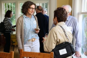 Two people engaged in casual conversation while holding drinks at a bright indoor social gathering.