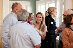 A group of people having an animated conversation in a bright interior room with mint green walls.