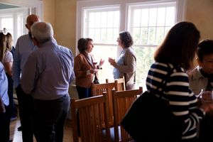 Group of people socializing and mingling during a casual indoor gathering with sunlight streaming through windows.