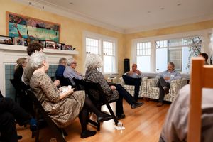 Group sitting in a bright living room with hardwood floors and windows during a casual gathering.