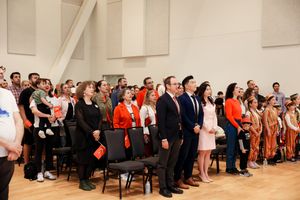 A large diverse group of people standing together in formal attire at an event in a bright auditorium space.