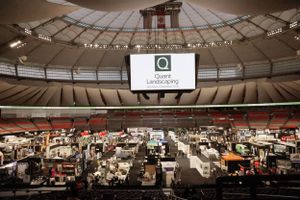 Large indoor stadium converted into temporary mass housing with rows of partitioned spaces and a central overhead display screen.