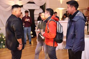 A group of people having a conversation at an indoor event with draped walls and decorations.