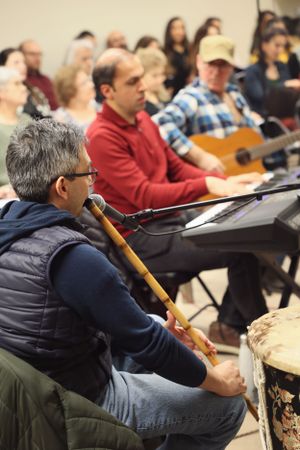 Musicians perform together during a group session with one playing percussion and others sitting with instruments in background.
