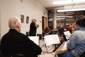 Musicians rehearse with their instruments while following sheet music during an indoor orchestra practice session.