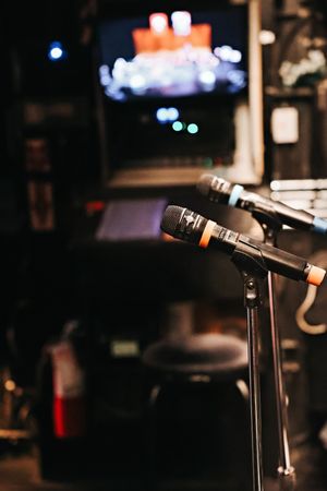 Professional microphones mounted on stands in a dark venue with blurred stage lighting in the background.