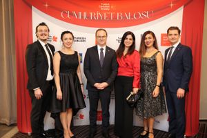 A group of formally dressed people pose together in front of a red backdrop at an event.
