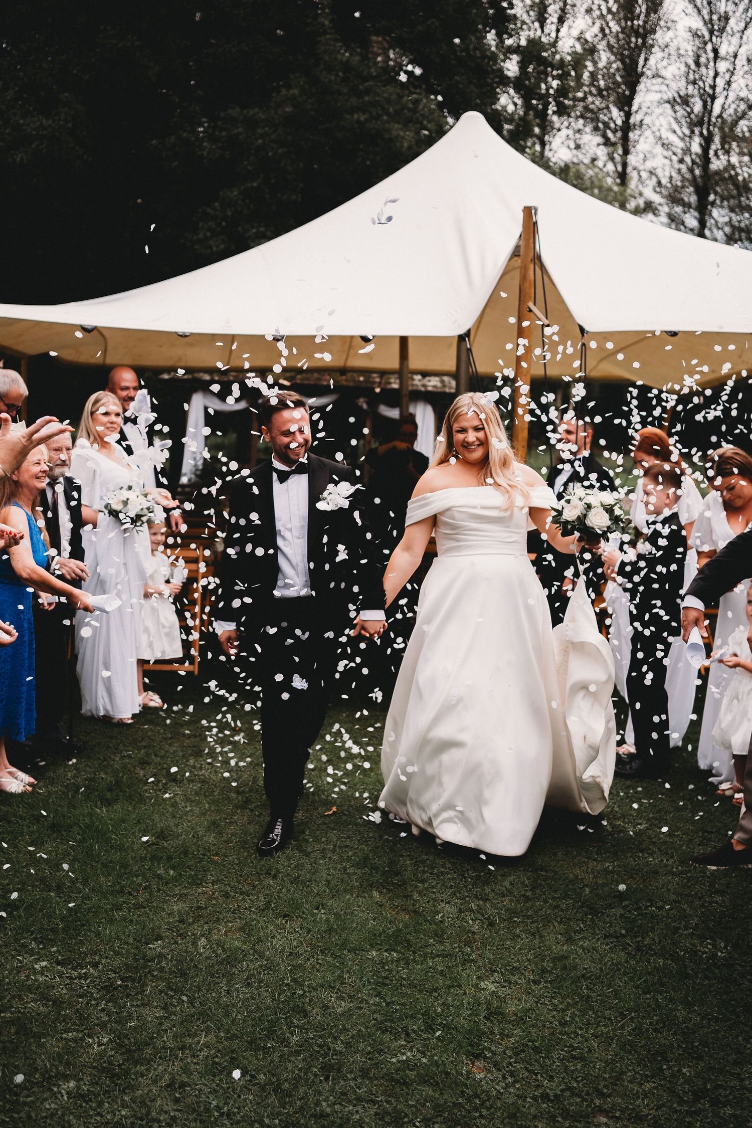 Wedding celebration with confetti being thrown outside a white tent canopy during an outdoor ceremony.