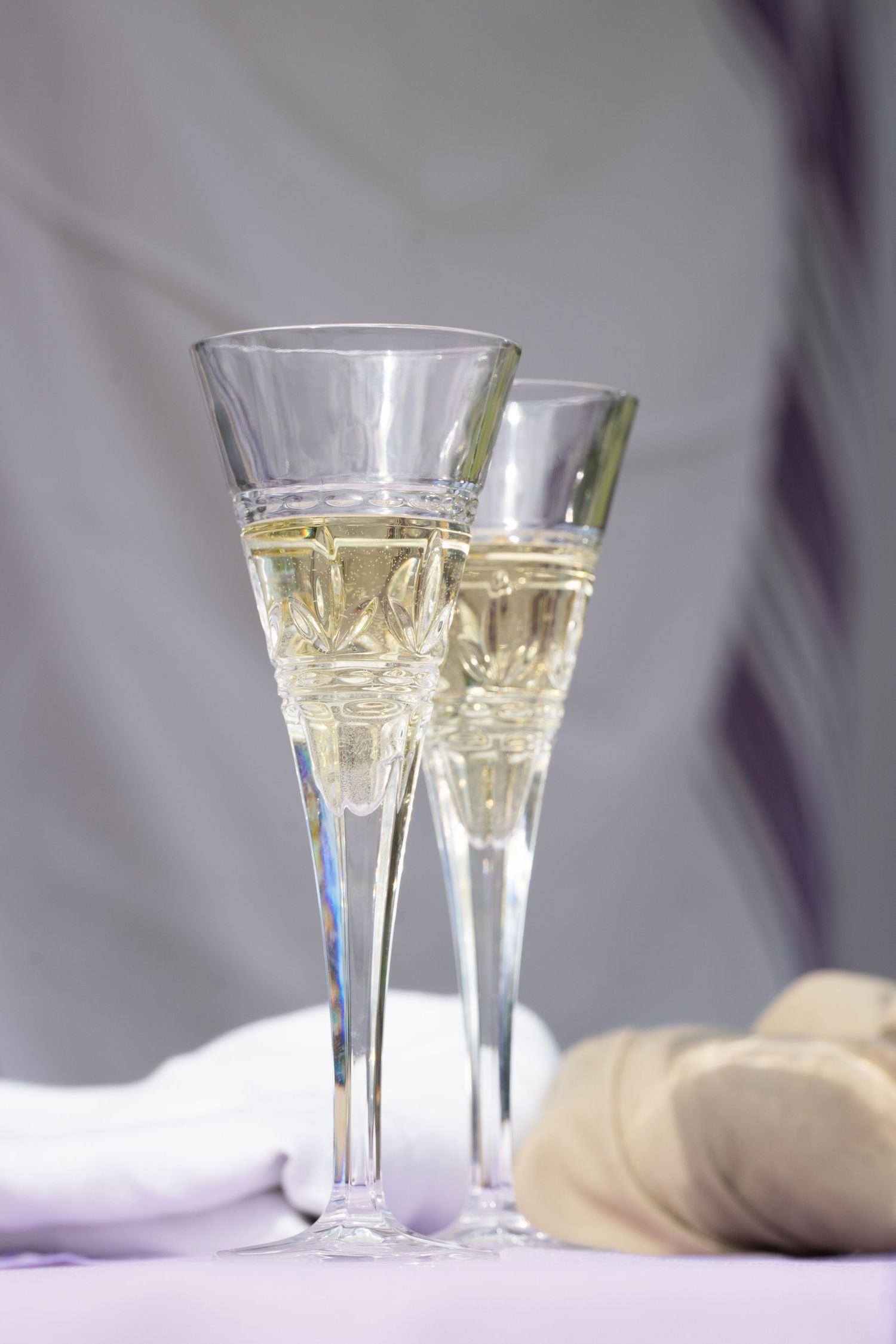 Two elegant champagne flutes filled with champagne on a light purple tablecloth at a wedding.