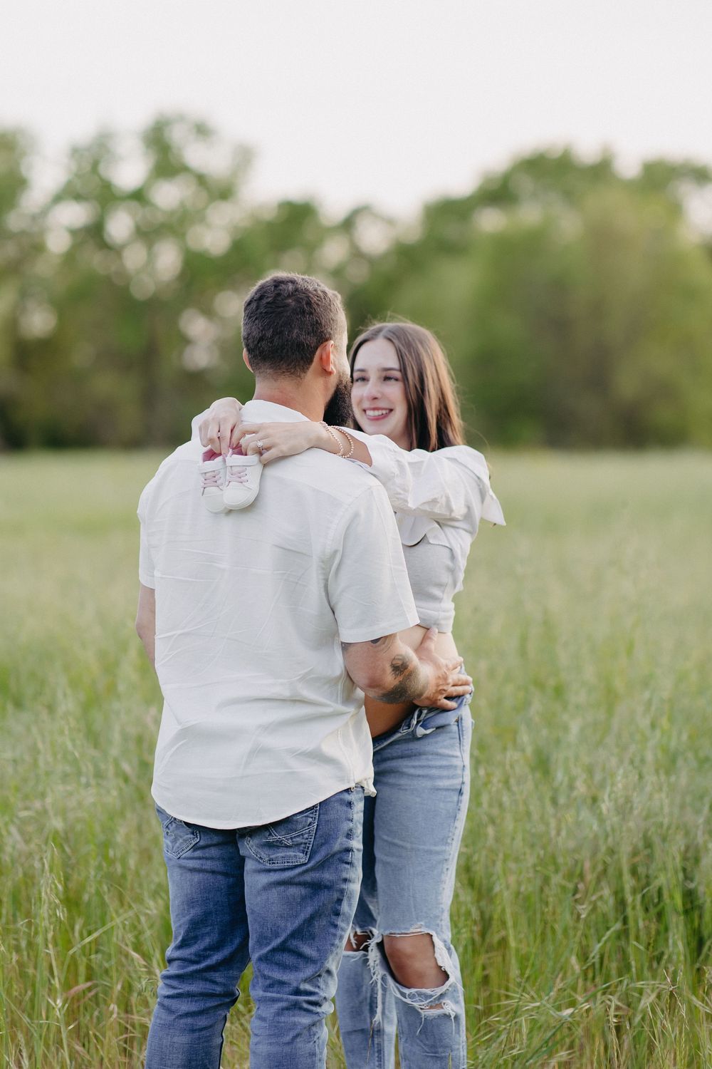 A romantic couple sharing an embrace in a sunlit meadow wearing casual white tops and denim.