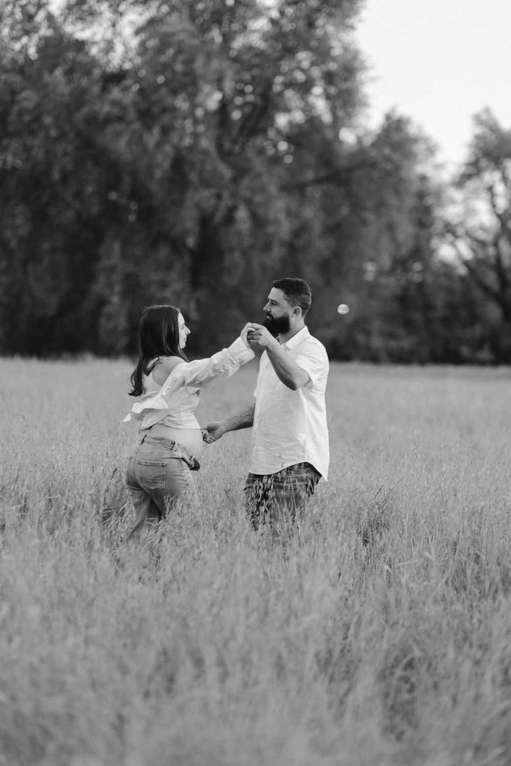 Black and white photo of a couple playfully dancing together in a tall grass field.
