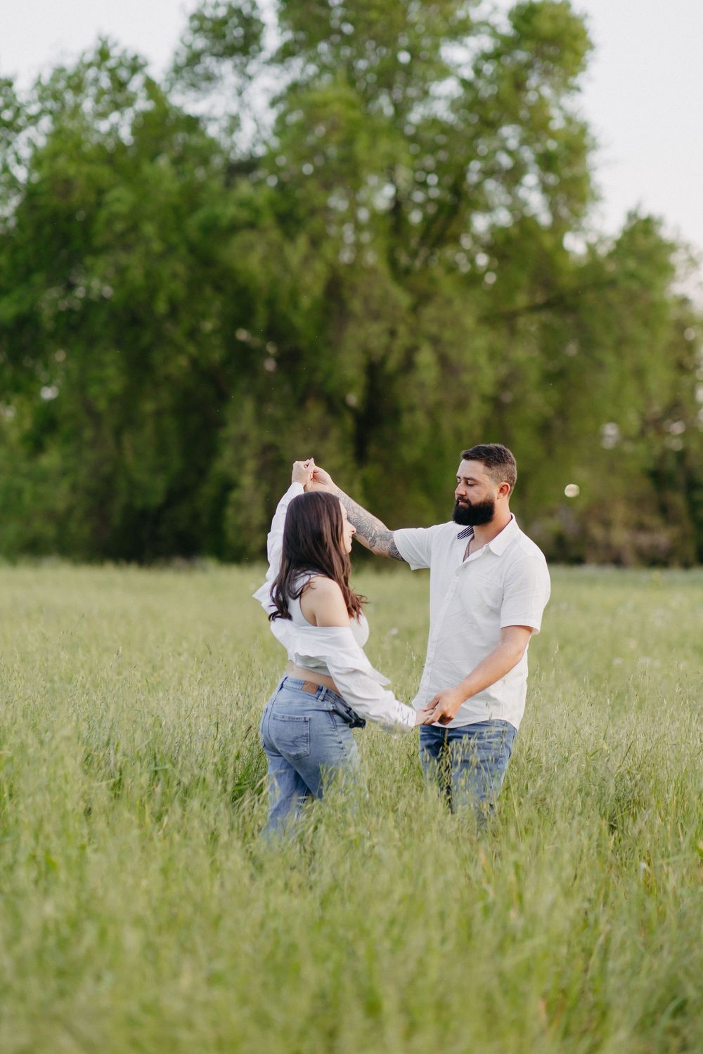 A couple dances together in a sunlit meadow wearing white and denim outfits.