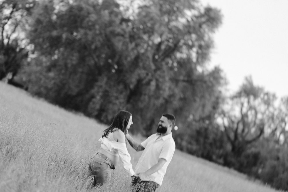 A couple dances together in a black and white photo taken in an open field with trees in the background.
