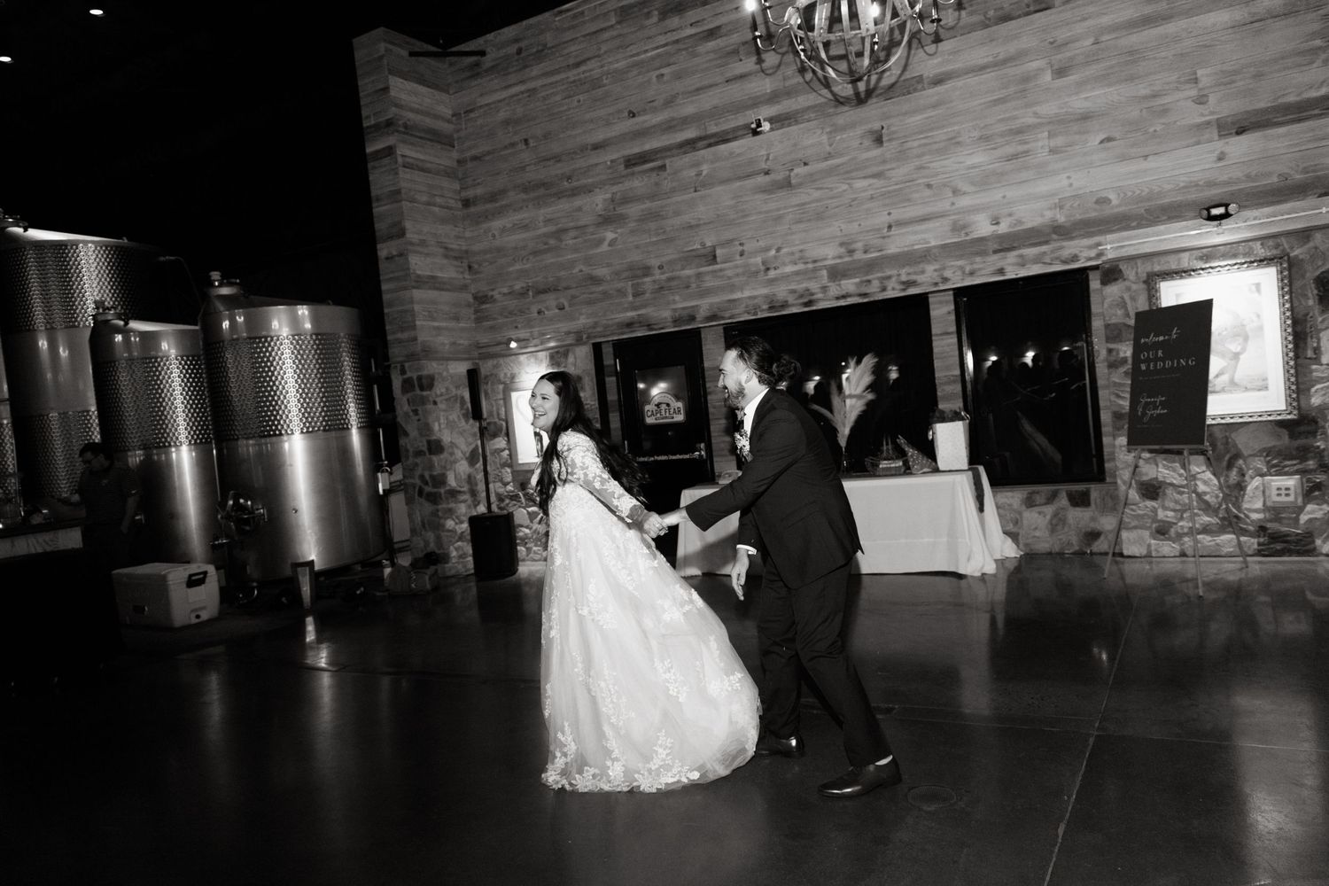 Two people share a romantic dance together in a rustic venue with wooden walls and dim lighting during a wedding celebration.