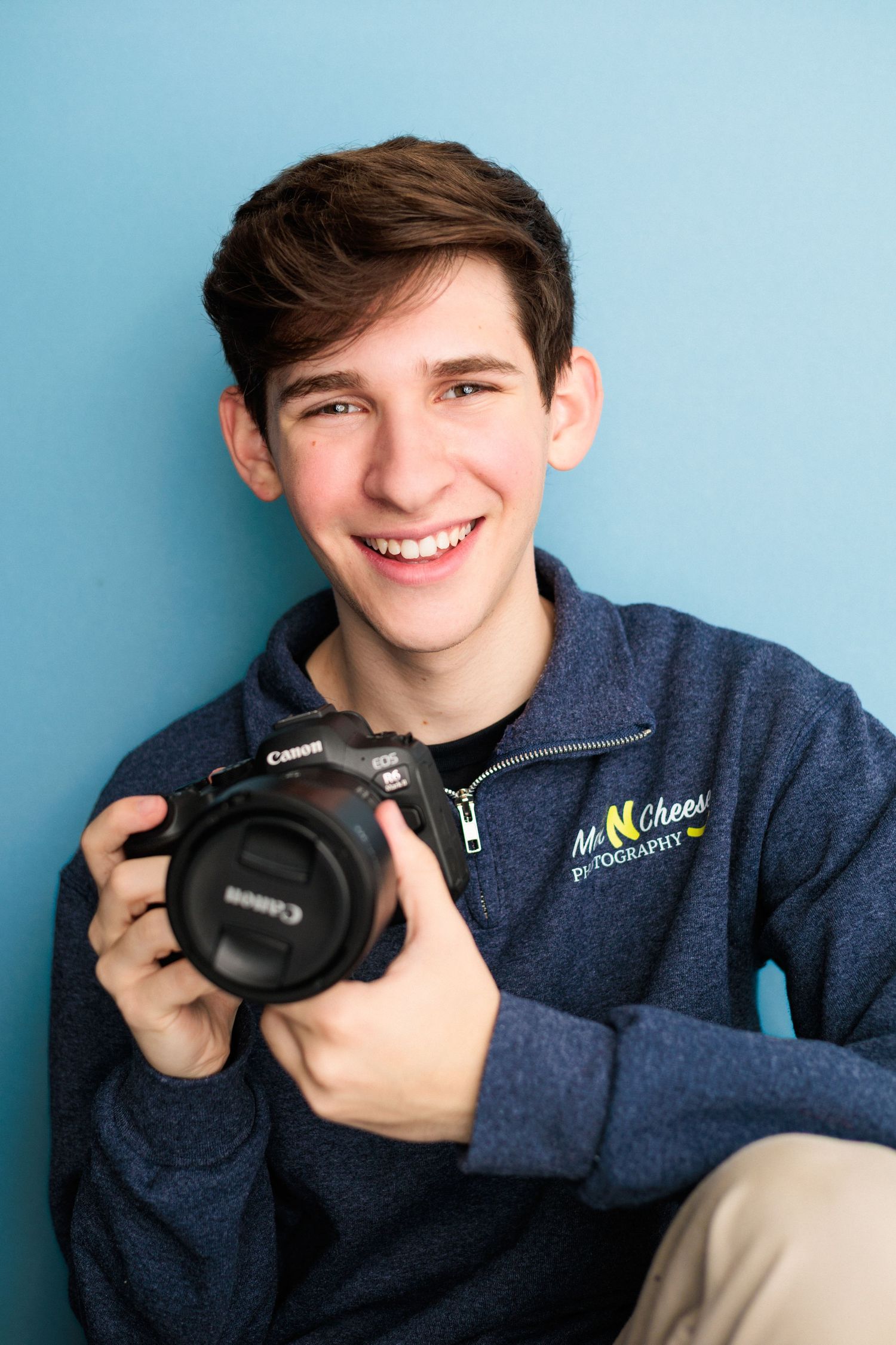A young teen boy with dark hair smiles in a maroon quarter-zip pullover against a teal background.