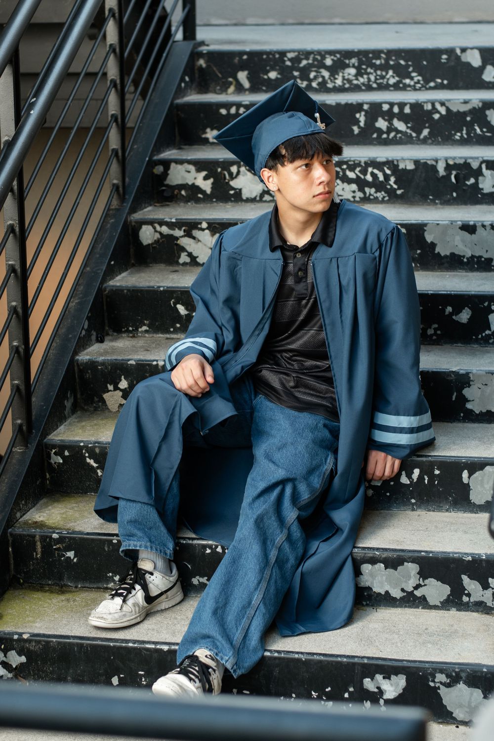 A person in a blue uniform and cap sits casually on concrete stairs wearing white sneakers.