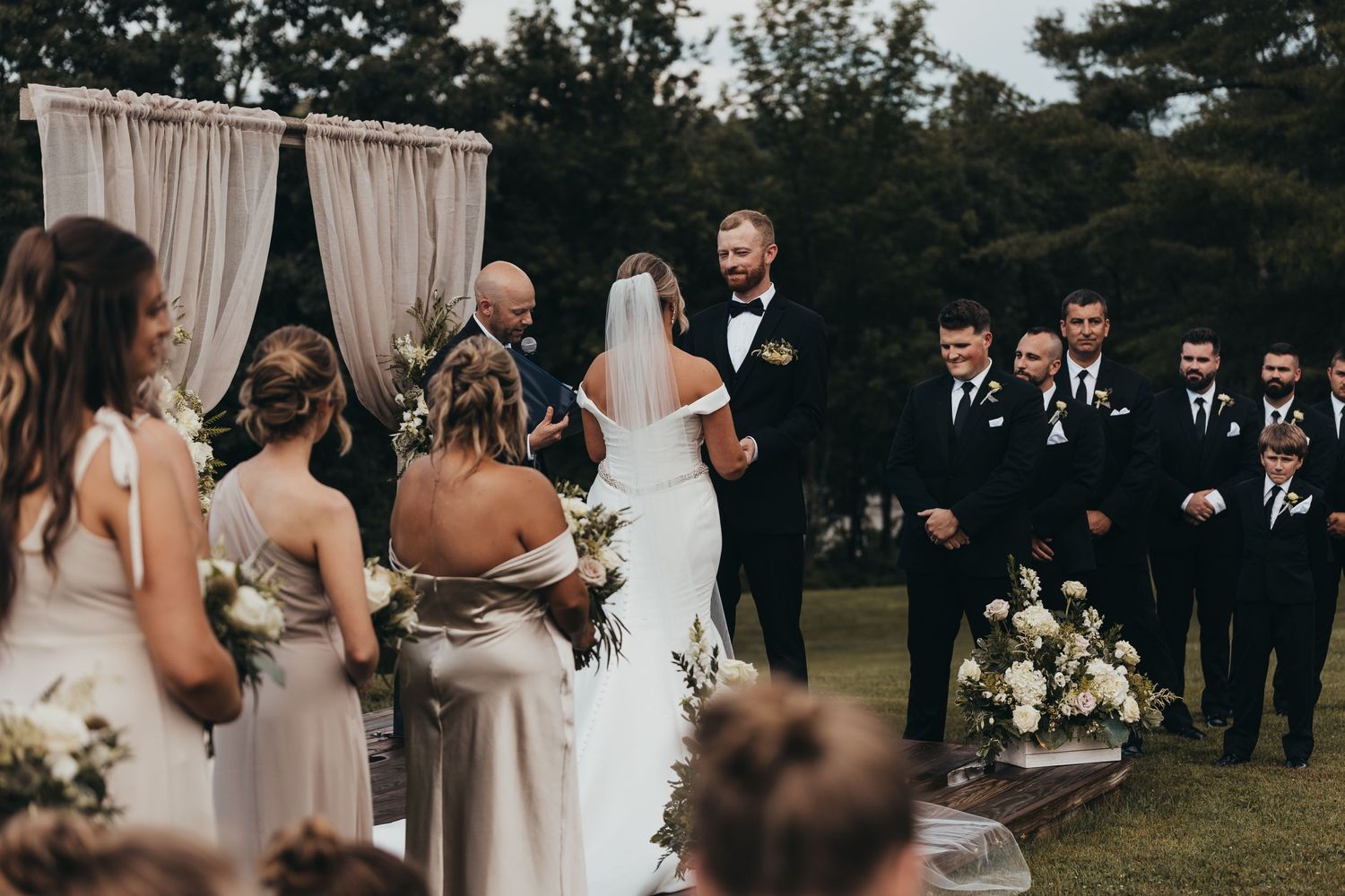 An elegant outdoor wedding ceremony with guests seated in rows among trees.