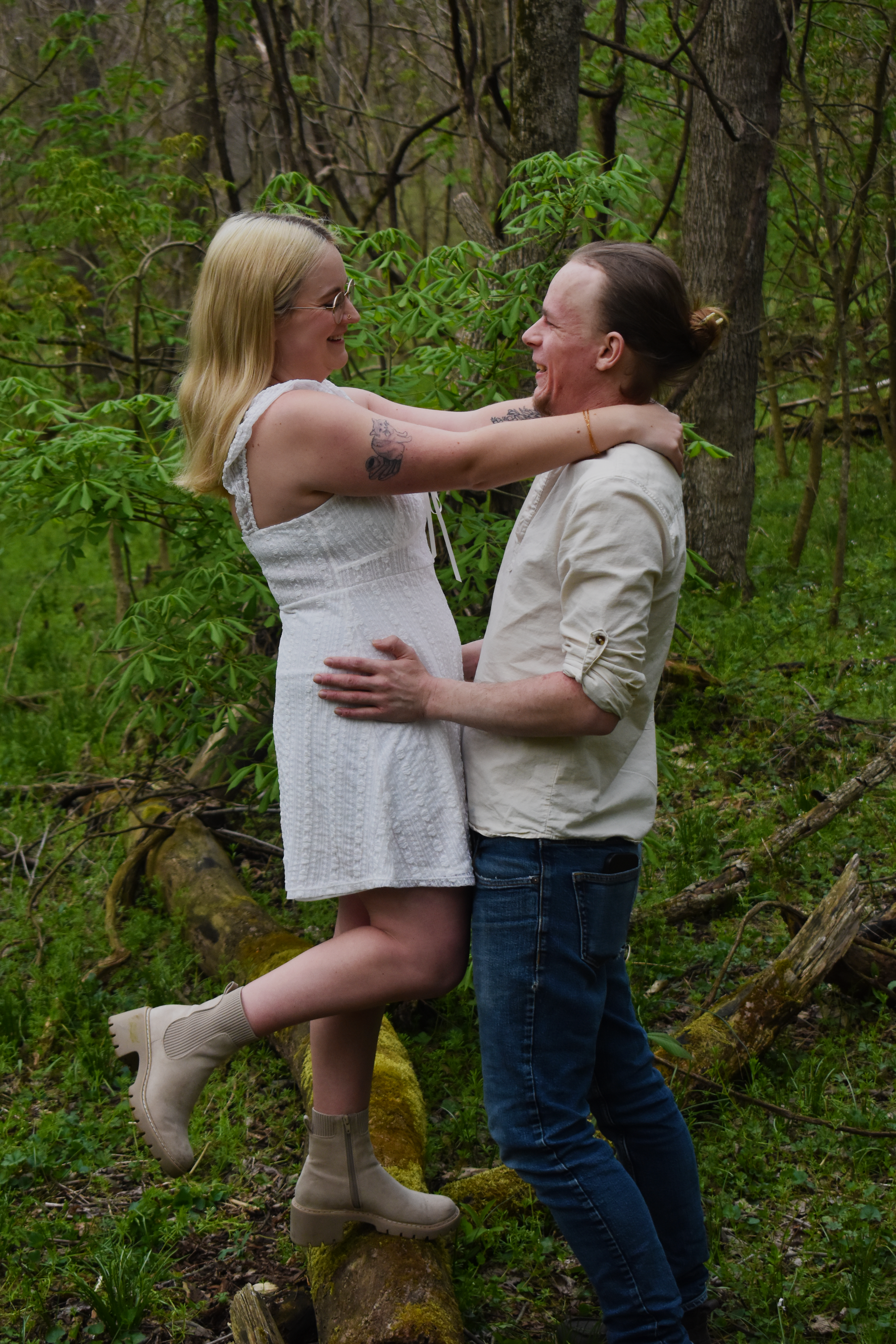 A couple sharing an intimate embrace while standing in a wooded area with green foliage in the background.