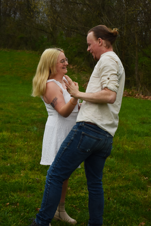 A joyful couple dances together on grass in a casual outdoor setting.