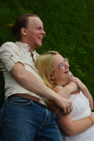 A happy couple laughs together while laying in green grass on a sunny day.