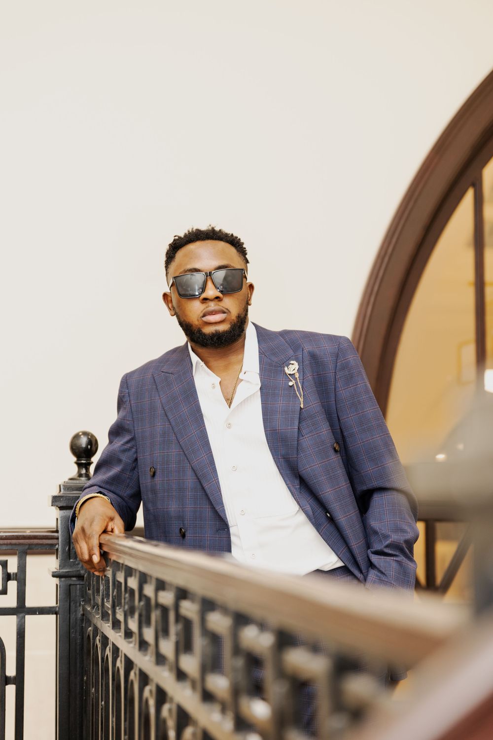 Stylish person in blue blazer poses along railing wearing sunglasses.
