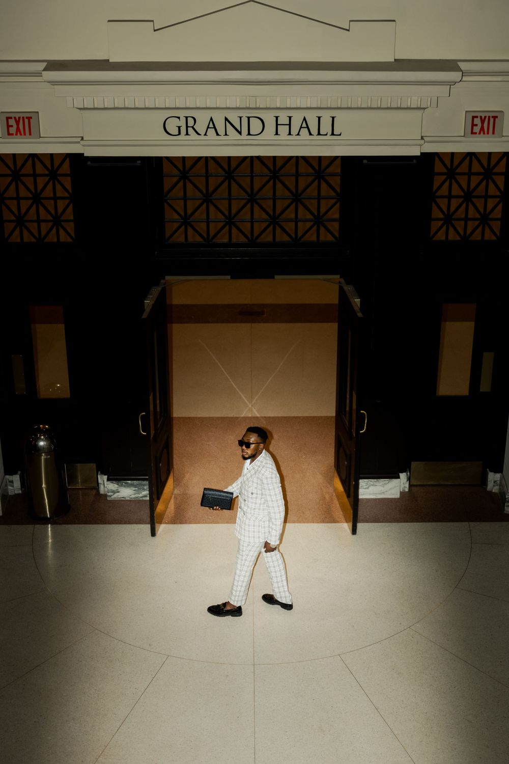 Person in white suit walks through spotlit grand hall.