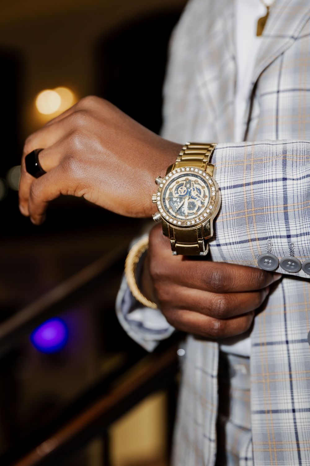 Close-up of gold luxury watch on person wearing light colored suit.